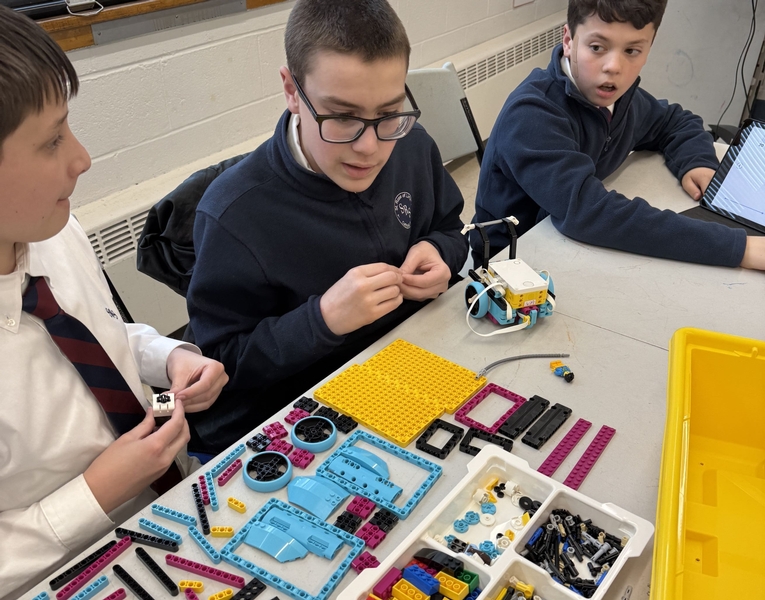 Three students sit at a table with an assortment of plastic parts that snap together into a robot.