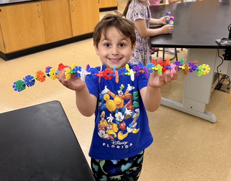 A young student holds up a long strip of interlocking plastic building pieces