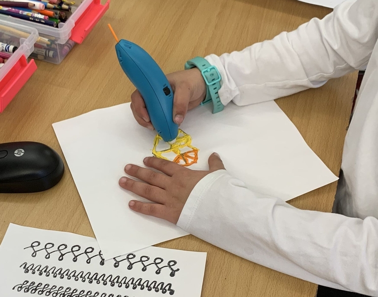 A child's hands are seen drawing a small shape on a white piece of paper with a 3D pen.
