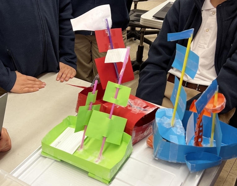 Three small boats made of paper tape and straws sit on a table