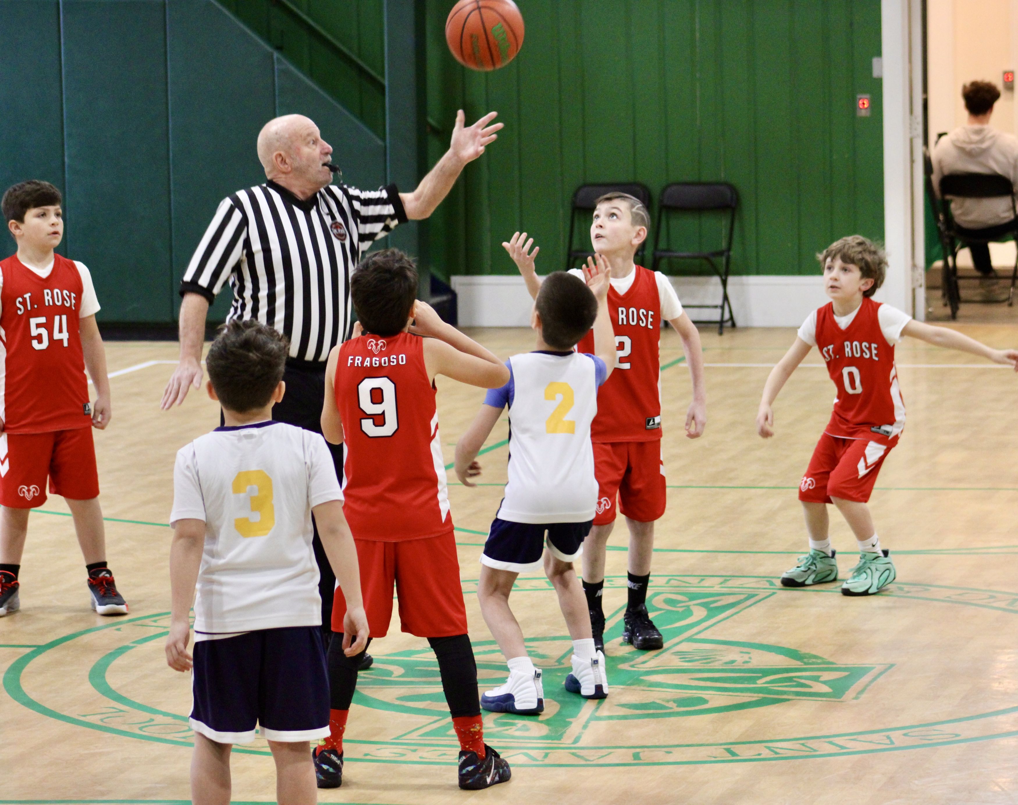 Boys from St. Rose and another school watch the airborne ball in a tip-off
