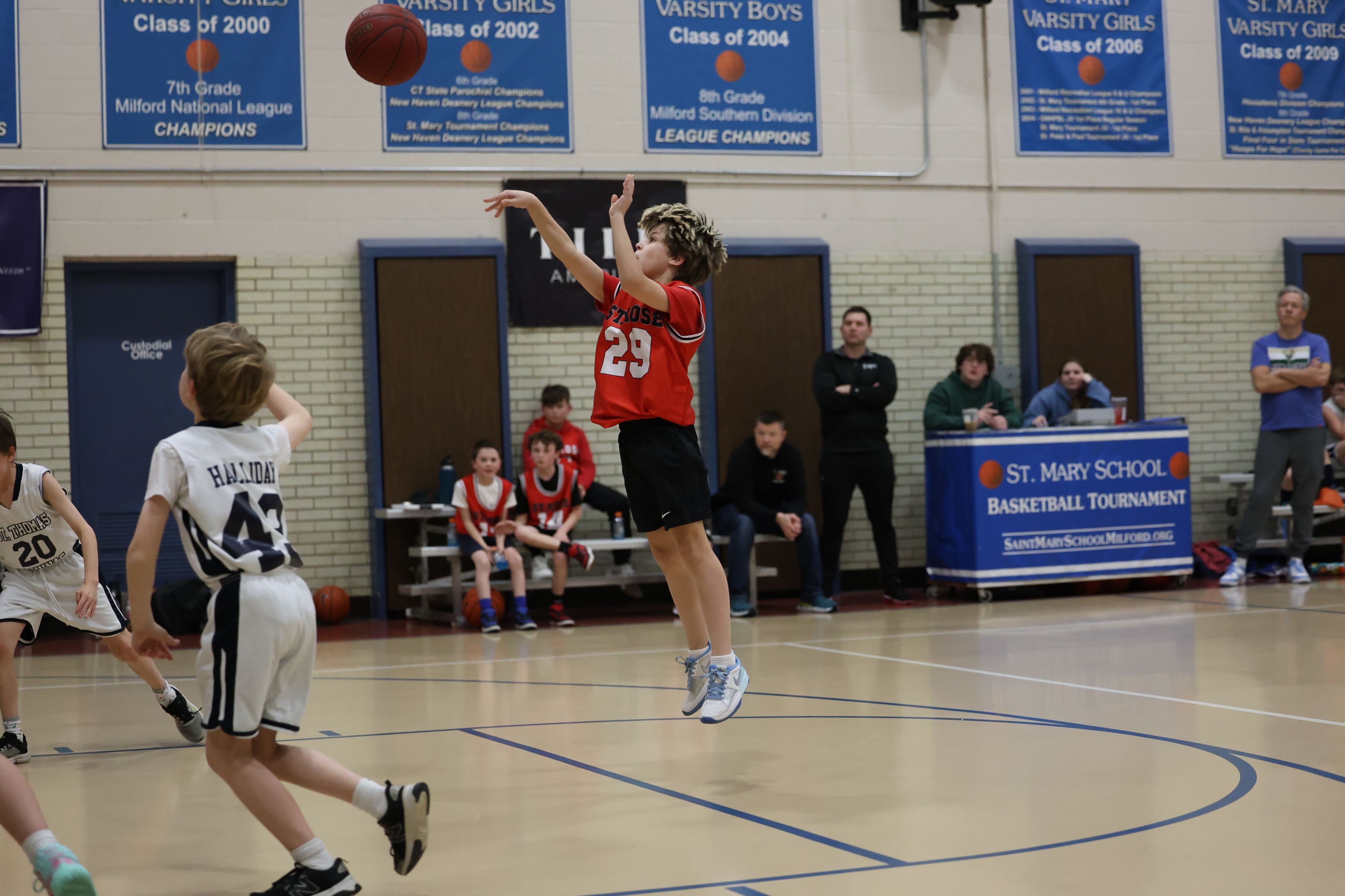 A boy is jersey 29 is jumping in midair, having just taken a shot at the hoop