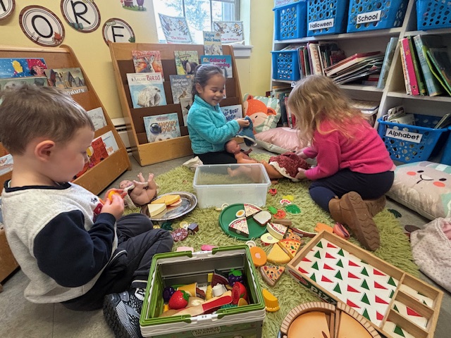 Thre preschool students feed play food to baby dolls